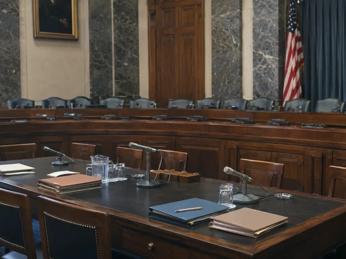 A closer documentary view of an empty 1970s congressional hearing room with witness microphones and folders.