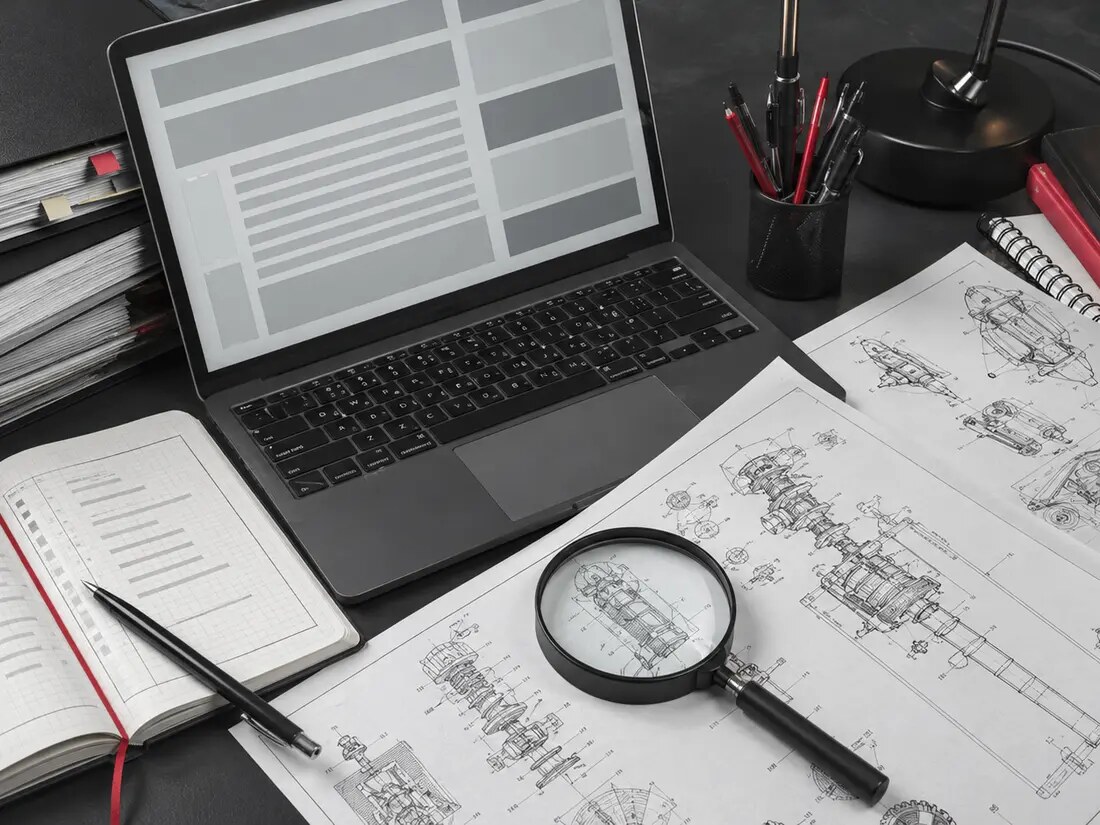A closer documentary view of a patent research desk with line drawings, citation notebook, magnifier, and laptop.
